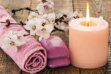 Soap with towel for bathroom procedures and  burning candle with flowering branch of apricot tree