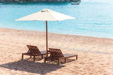 Beautiful sea summer beach. Wooden chairs and umbrella on sandy and pebble beach by blue sea. Holiday, travel and vacation concept.