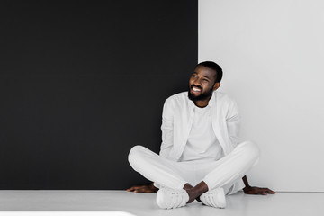 smiling stylish african american man sitting on floor near black and white wall