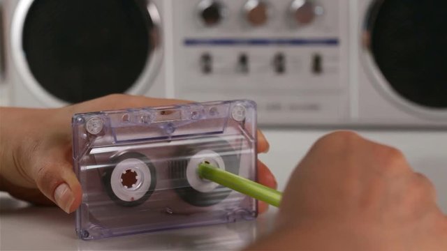 Woman hands rewind an audio cassette using a pen - retro player in background, camera zooming or closing in, closeup