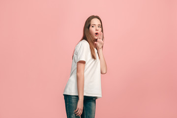 The young teen girl whispering a secret behind her hand over pink background