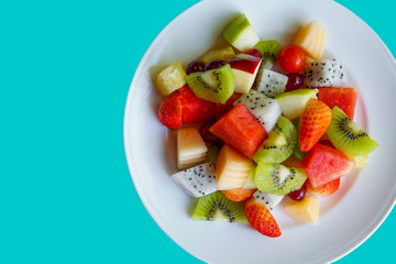 Fresh tropical fruit salad with strawberry pineapple  melon kiwi grapeand dragon fruit on green pastel background. Flat lay, top view for healthy.