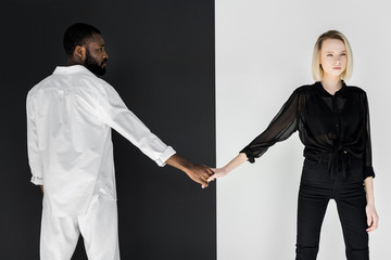 african american boyfriend and blonde girlfriend holding hands near black and white wall