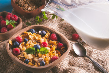 Cornflakes and other cereals with fresh fruits of raspberries, blueberries and pouring milk on healthy breakfast.