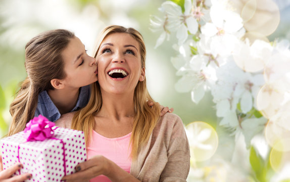 people, holidays and family concept - daughter kissing happy mother and giving her birthday present over cherry blossom background