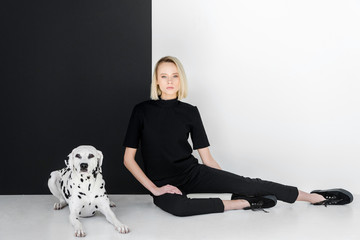 attractive stylish blonde woman in black clothes sitting near black and white wall with dalmatian...