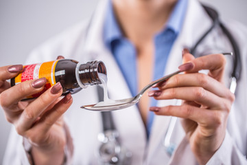Hands of young woman doctor pouring medicinal syrup on spoon