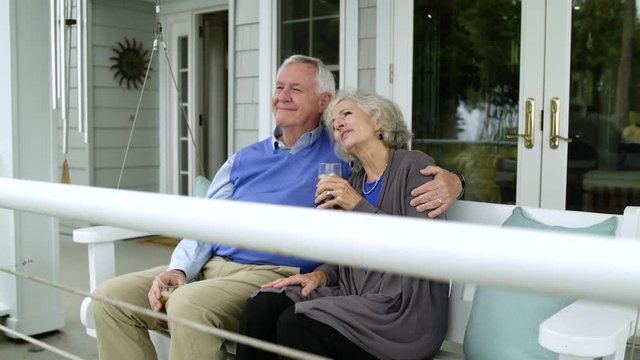 Couple sitting on swing seat on porch chatting.
