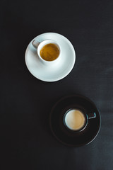 high angle view of black and white cups of milk and coffee on black surface