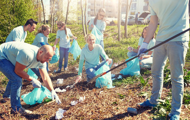 volunteering, charity, people and ecology concept - group of happy volunteers with garbage bags and rake cleaning area in park