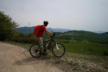 A young man on a bicycle looks at the mountains visible in the distance