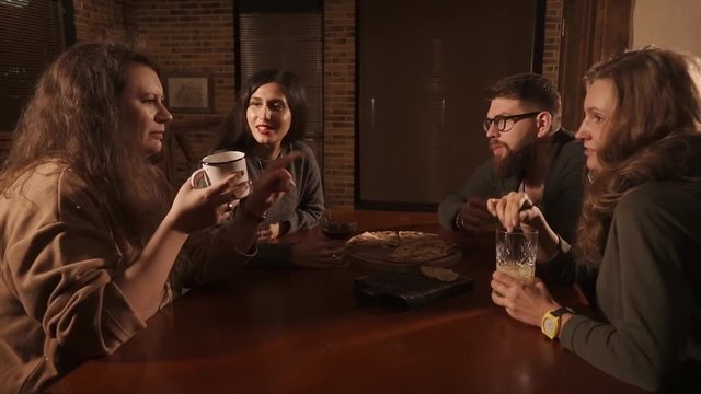 Informal meeting of colleagues in a pizzeria in evening time. People are drinking beverages telling funny stories to each other