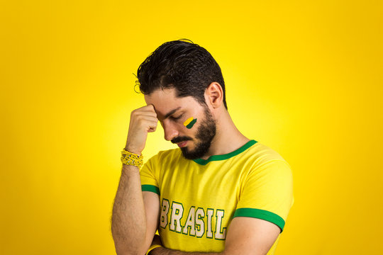 Brazilian supporter of National Team of football is looking down, depressed, worried.