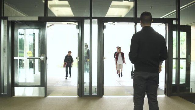 Medium shot of security person standing while students enter from front door