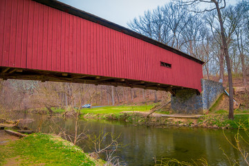 Outdoor view of red covered bridge inside of the forest over a small river in Lancaster