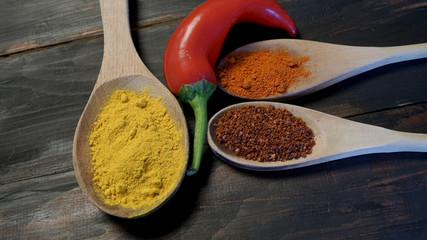 Close up turmeric, paprika, pepper flakes on wooden spoons with red hot chili peppers.