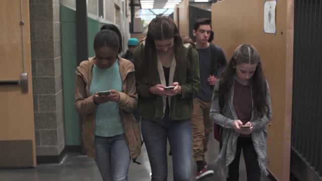 Medium shot of a group of girls on a school corridor texting