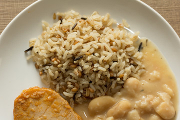 Pork chop, Brown rice and white beans. White dish on wooden table. Overhead close up of food dish.