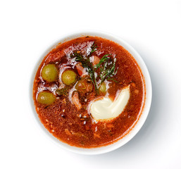 Tomato soup with meat, cucumbers and olives in white bowl on white background. Top view.