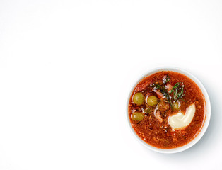 Tomato soup with meat, cucumbers and olives in white bowl on white background. Top view.