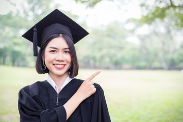 Portrait of young asian woman outside the building on her graduated day. Cute asian girl with her hand finger point to copy space area, Education success graduate concept