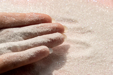 Fototapeta premium Hand with glitter sand - pastel pink glitter background with selective focus - glitter powder - copy space