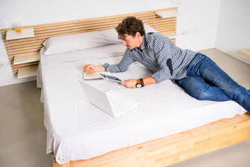 Young man in bed checking his tablet and notes