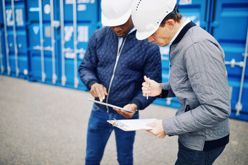 Engineers standing in a shipping yard comparing inventory lists