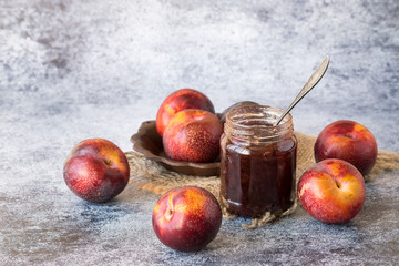 Fresh large ripe plums and a small glass jar with jam on a blue background.