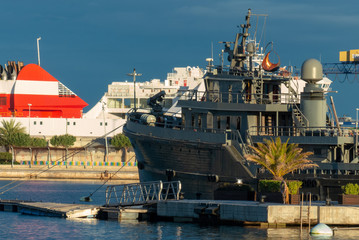 A gray classic boat moored in the port of Valencia with the ferry in the background with blue sky...