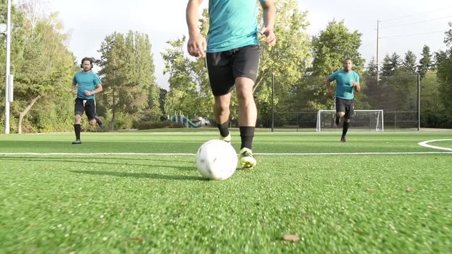 Male soccer players playing soccer with man dribbling ball ahead.