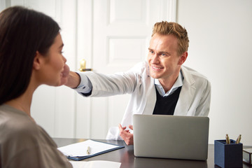 Male cosmetologist touching woman face at laptop in salon