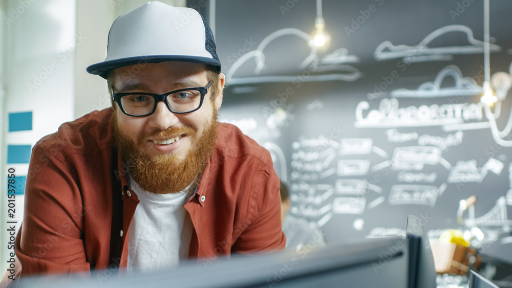 Poster Smiling Beautiful Man Mobile Vide Game Developer in a Cap Looking at The Monitor. Young People Work at the Creative Development Studio.