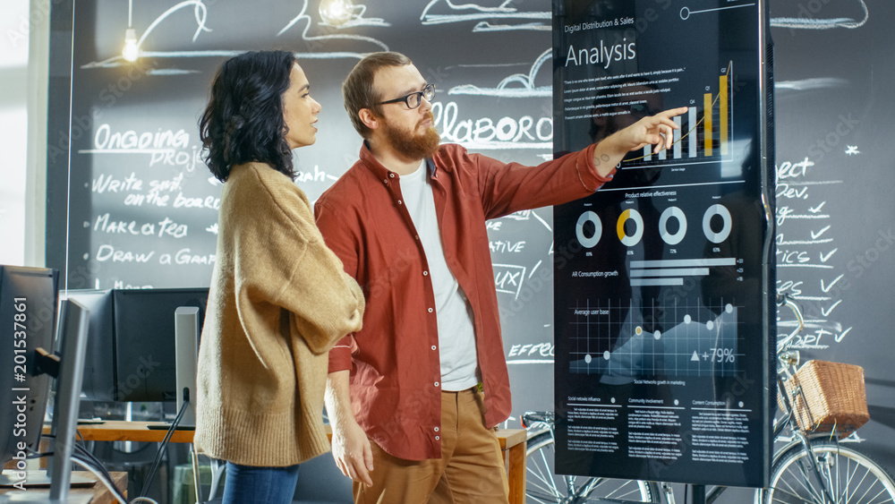 Poster Female Developer and Male Statistician Use Interactive Whiteboard Presentation Touchscreen to Look at Charts, Graphs and Growth Statistics. They Work in the Stylish Creative Office.