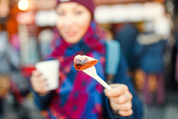 Woman eating sausage with hot wine on the central square in European town. Concept of street food at winter time near tourist attractions