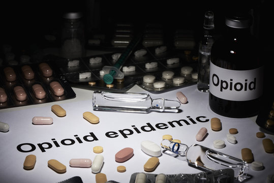Im Dunkeln sieht man eine Ampulle Opioid daneben liegt ein zettel auf dem in Englisch Opioid Epidemie geschrieben ist. Drumherum liegen viehle tabletten und Spritzen verstreut.