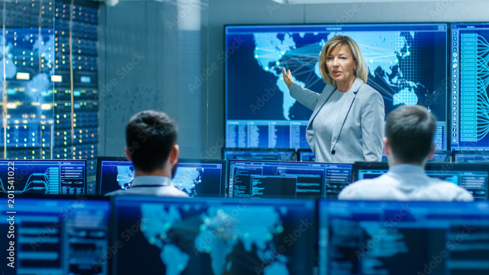 Poster in the system monitoring room senior female engineer holds briefing for her subordinate specialists,