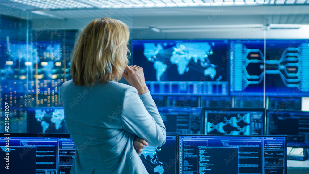Poster In the System Control Room Female Head of the Department Crosses Arms and Thinks Standing with Her Back to the Camera. In the Background Multiple Screens Showing Interactive Data.