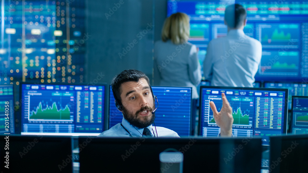 Poster Stock Exchange Trader Makes a Deal with Big Client Over the Headset. He Works with Other Brokers and is Surround By Computers with Graphs and Ticker Numbers on Screens.