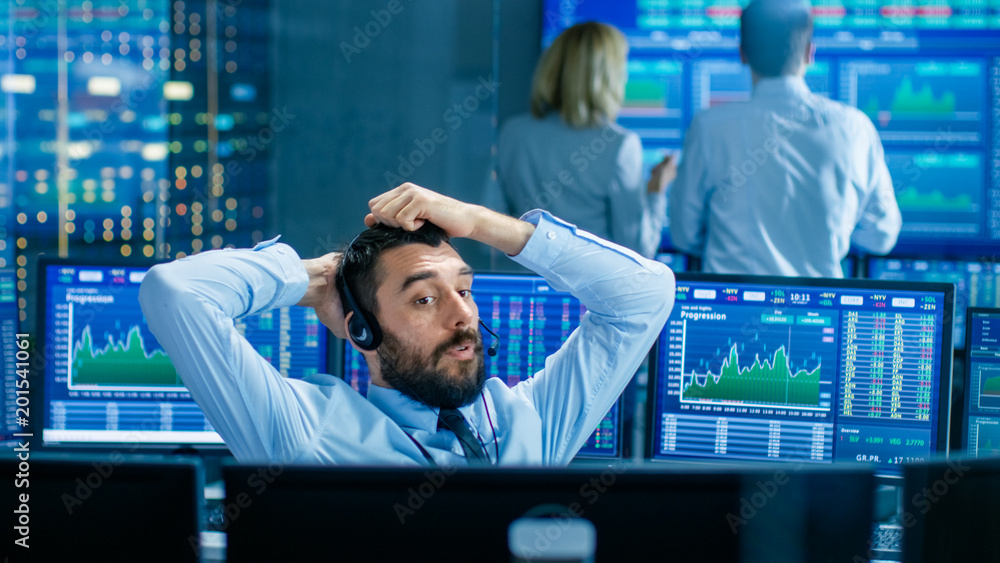 Poster Stock Exchange Trader Makes a Deal with Big Client Over the Headset. He Works with Other Brokers and is Surround By Computers with Graphs and Ticker Numbers on Screens.