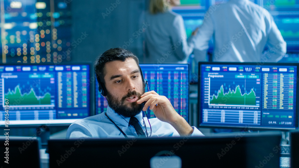 Poster Stock Exchange Trader Makes a Deal with Big Client Over the Headset. He Works with Other Brokers and is Surround By Computers with Graphs and Ticker Numbers on Screens.