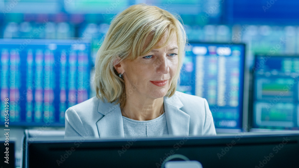 Poster Portrait of the Senior Female Stock Trader Operating at Her Workstation. Behind Her Multiple Monitors Showing Data, Ticker Numbers and Graphs.