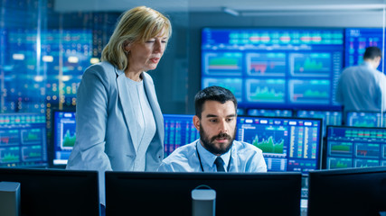 In the Stock Market Firm Head of the Department Talks with Professional Trader. They're Surrounded by Screens with Graphs and Ticker  Numbers.