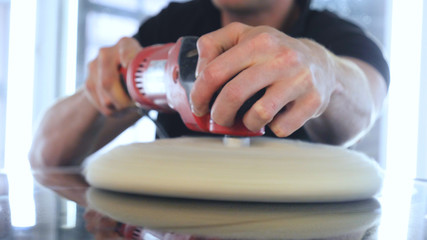 A young handsome guy, a professional worker polishes a black car, repairs cars, deterging, car washing, service.