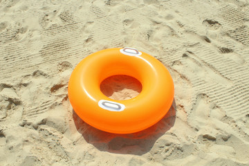 Obraz premium Orange children's circle for swimming on a sandy beach. Close-up.