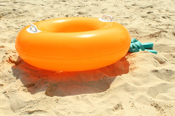 Orange swimming circle and blue female slates on beach sand. Close-up. Background.