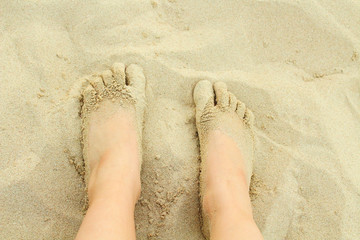 The legs of a child on the beach sand. Close-up. Background.