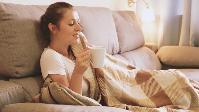 Young female is watching TV and sitting with tea at home.