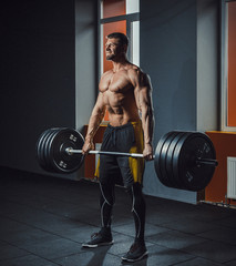 Fototapeta na wymiar european caucasian athletic man doing deadlift with heavy barbell. man lifting barbell opposite window. emotional moment of lifting weight. affective lifting in gym. posing in gym