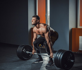 european caucasian athletic man doing deadlift with heavy barbell. man lifting barbell opposite window. emotional moment of lifting weight. affective lifting in gym. posing in gym